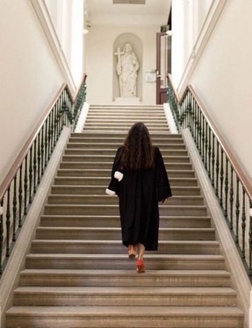 Avocate en Robe Noire : Carrière et Réussite au Palais Avocate en robe noire montant un grand escalier vers une statue dans un palais de justice.