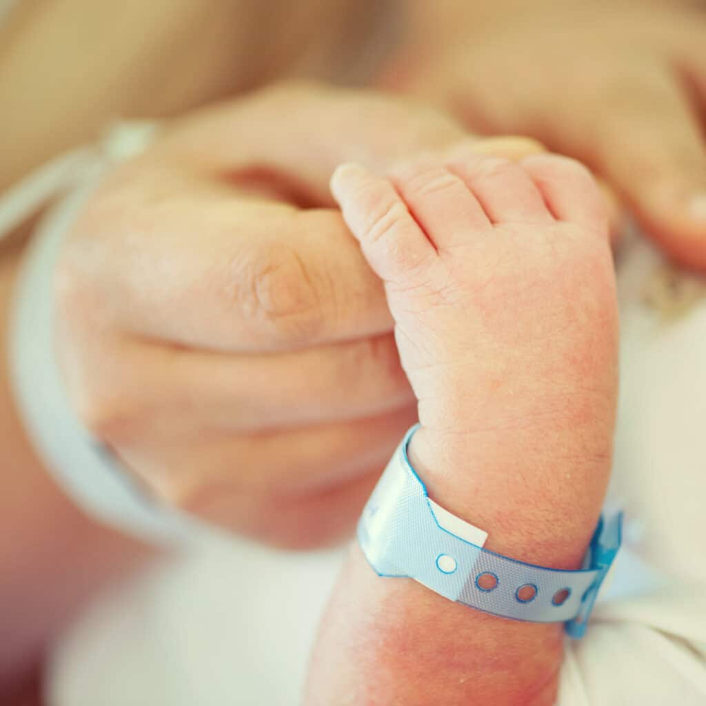 Nouveau-né et parent : premier contact à la maternité Main d'adulte tenant la main d'un nouveau-né portant un bracelet d'identification bleu à la maternité.