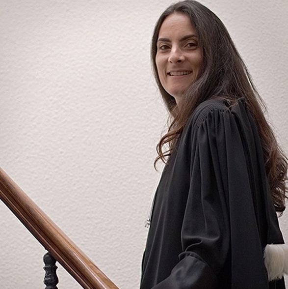 Femme avocate souriante en robe noire avec épitoge en fourrure blanche montant un escalier.